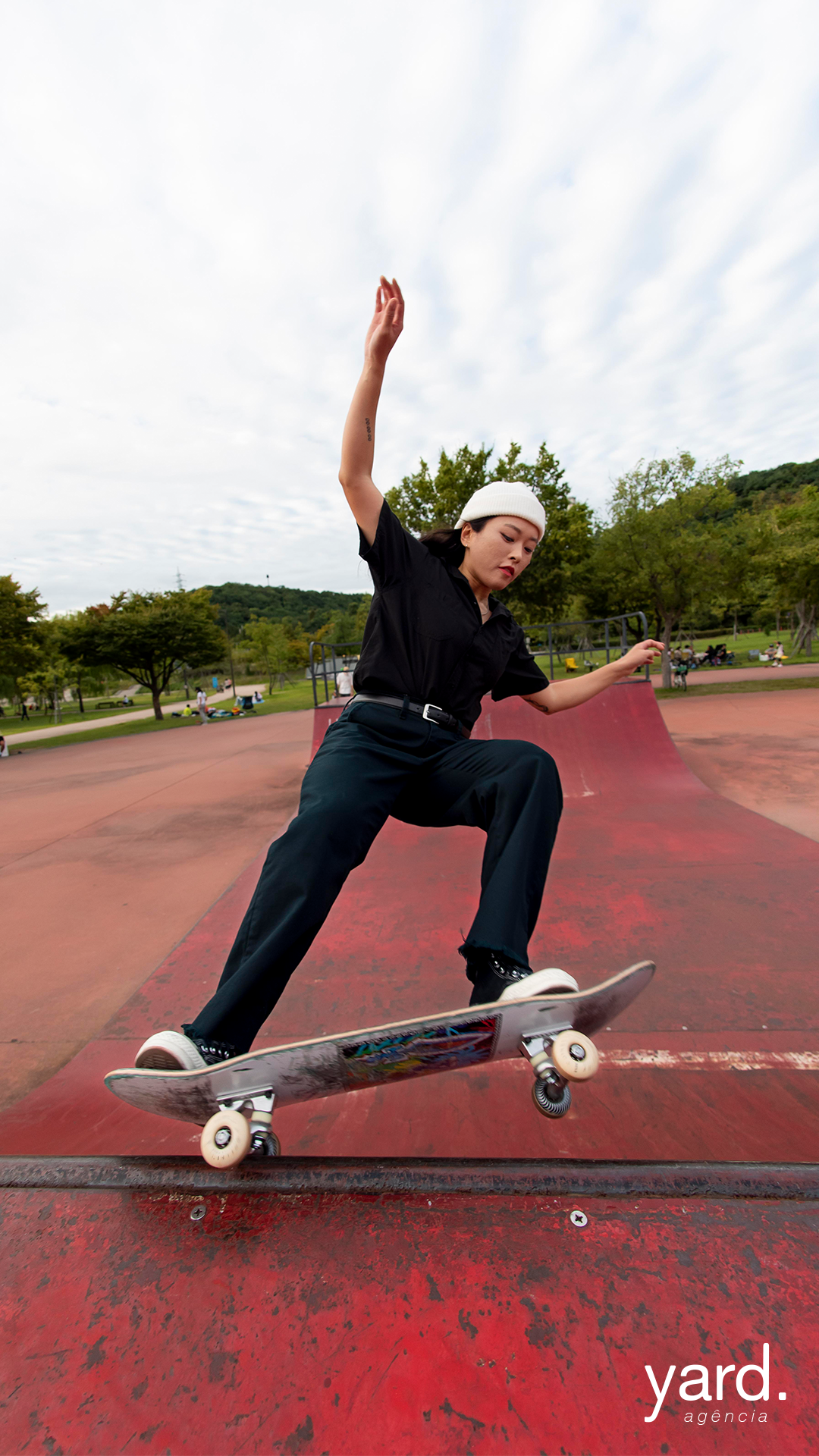 imagem em formato vertifical de uma menina fazendo uma manobra de skate em uma pista